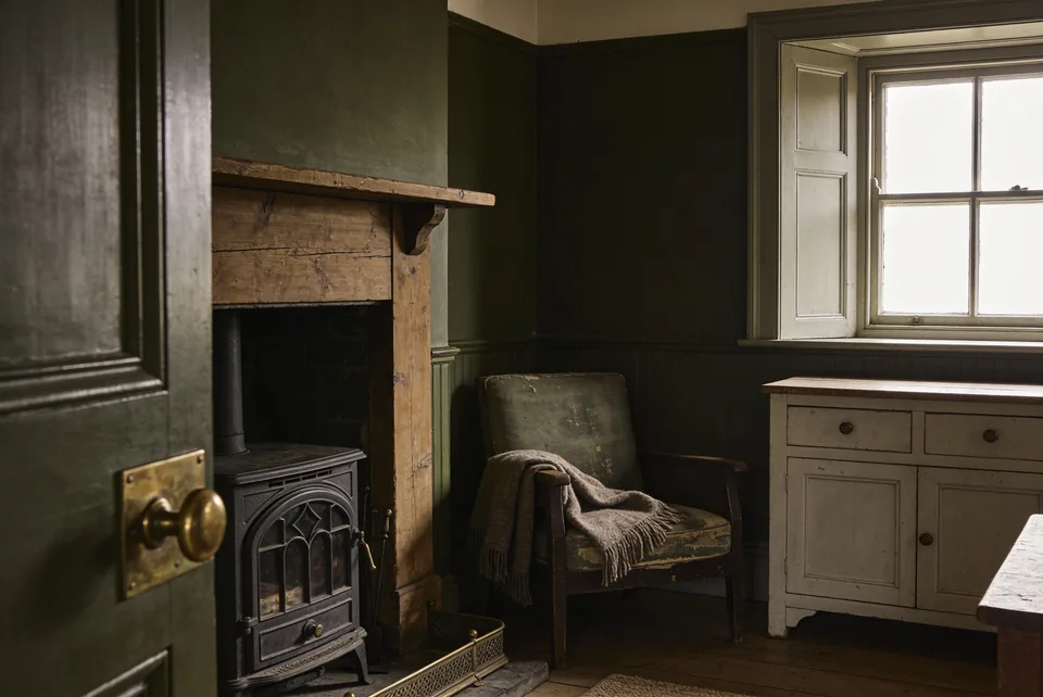 A lived-in cottage corner in low warm light — aged wood, worn brass, a quiet hearth